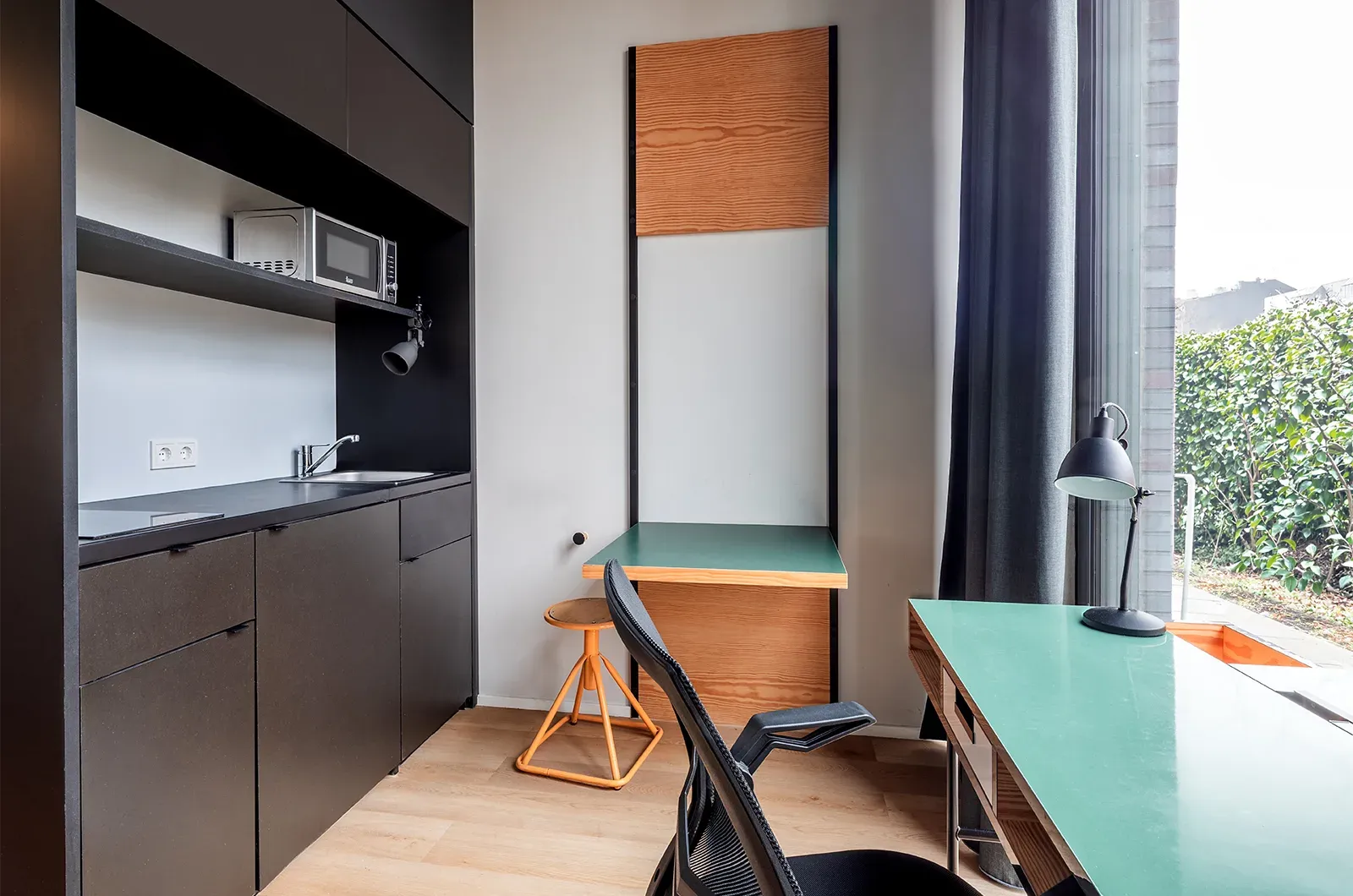 Undecorated desk, foldable table and kitchenette in a Classic Patio Room at Neon Wood Berlin Mitte-Wedding showing furnished baseline without styling accents