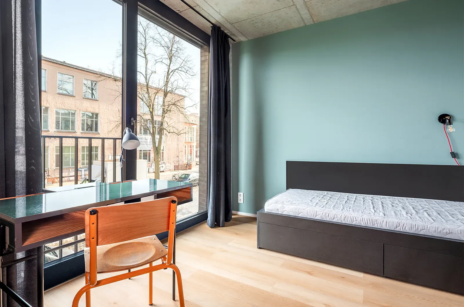 Undecorated bed, desk and outside view in a Deluxe Room at Neon Wood Berlin Mitte-Wedding showing furnished baseline without styling accents