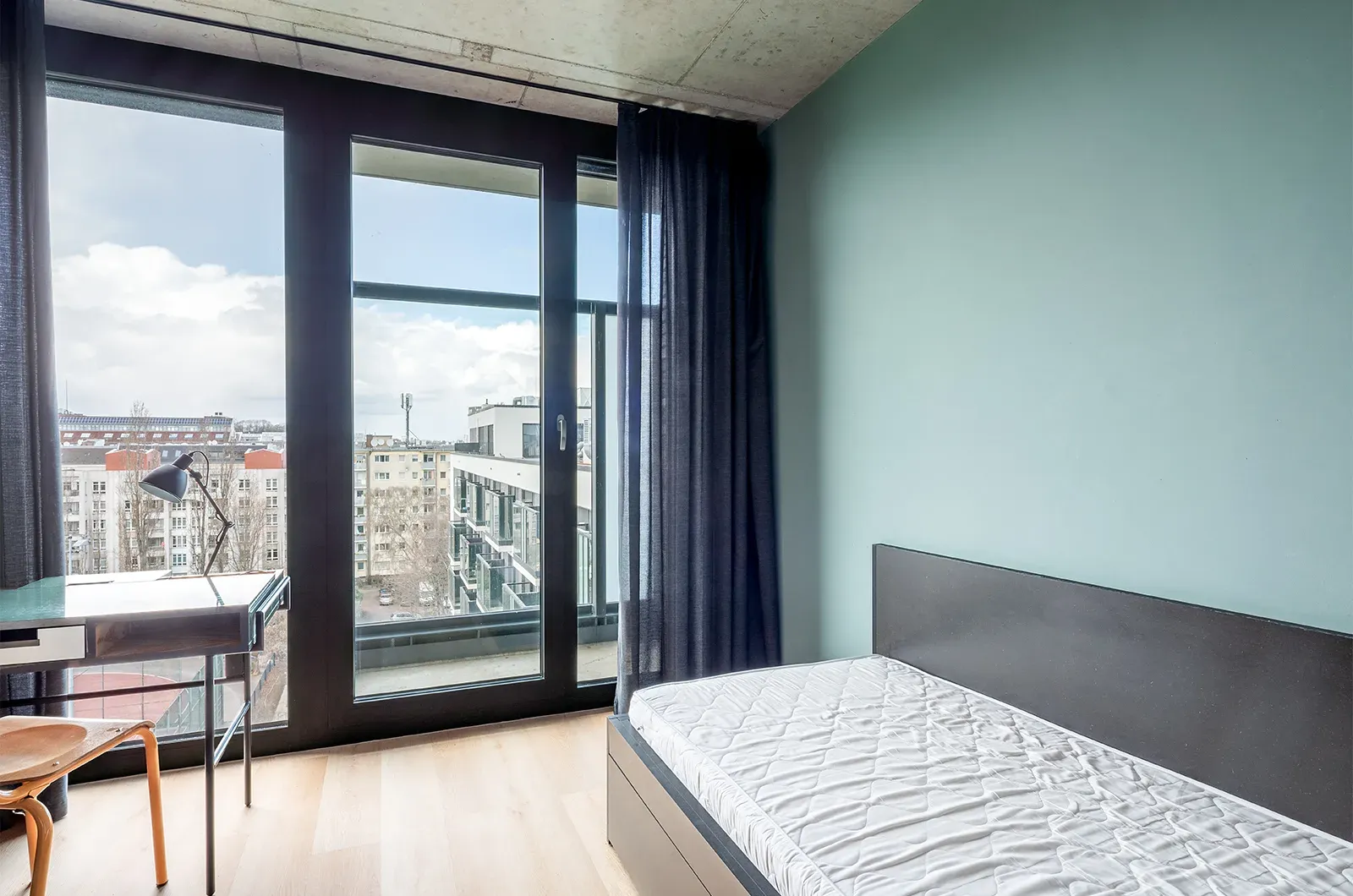 Undecorated bed area with view of the balcony and outside space in a Deluxe Balcony Room at Neon Wood Berlin Mitte-Wedding showing furnished baseline without styling accents