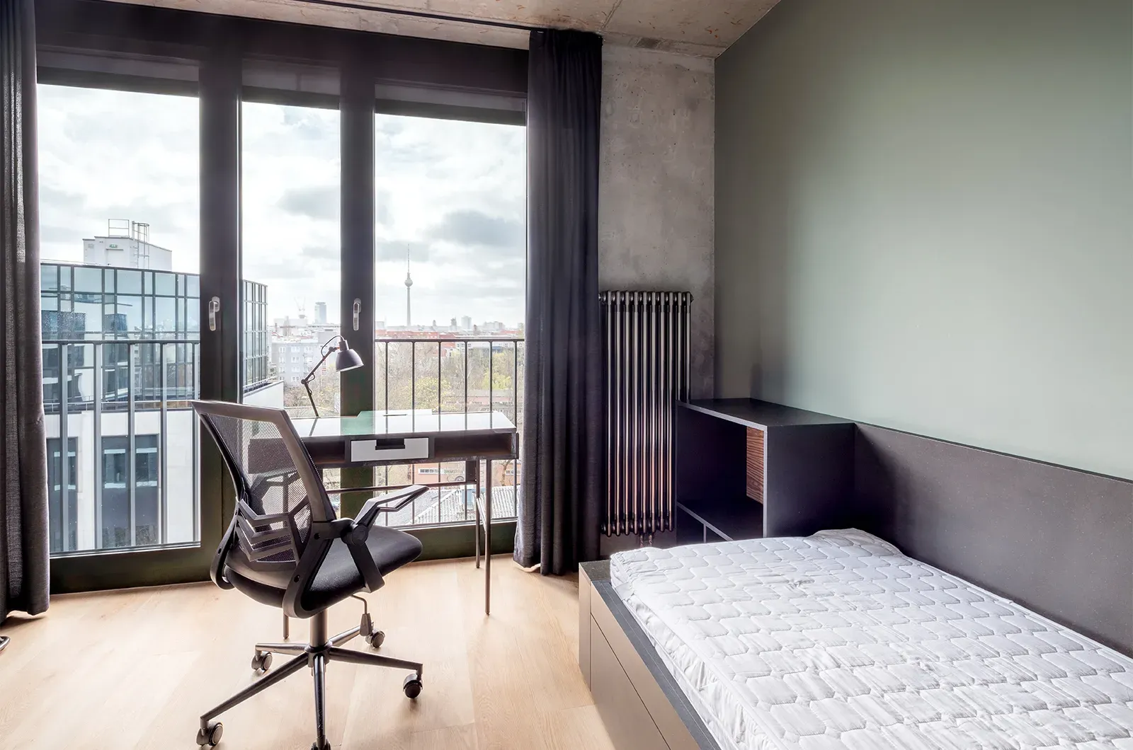 Undecorated bed, desk and outside view in a Penthouse Room at Neon Wood Berlin Mitte-Wedding showing furnished baseline without styling accents